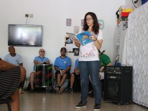 Na foto, a atriz Mariana da Cruz Martins Bressan está em pé lendo o livro Cuca, da Coleção Regionais